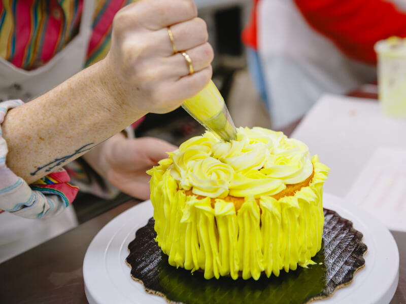 Person decorating a cake with yellow buttercream icing